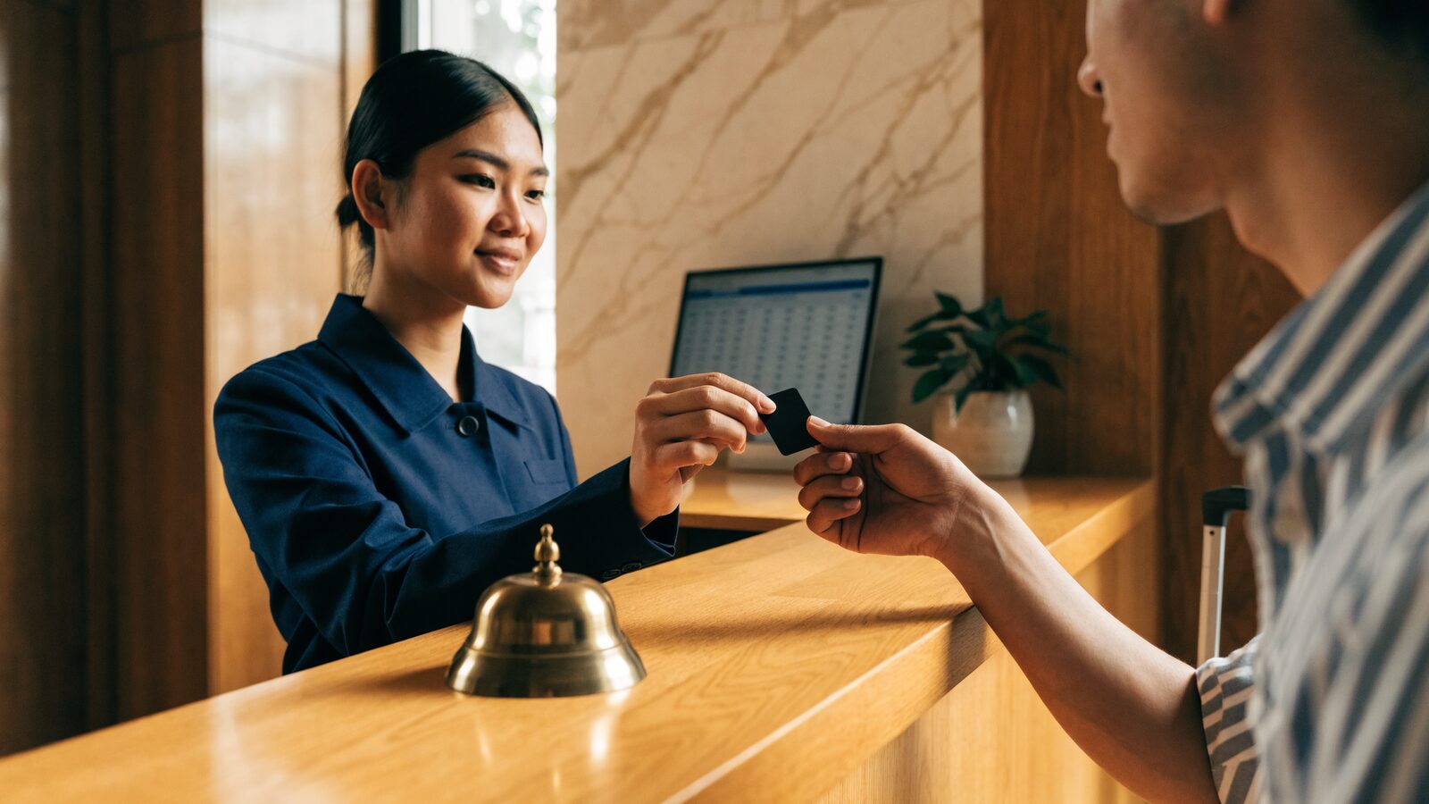 Front-desk agent handing a keycard to an arriving guest across the reception counter
